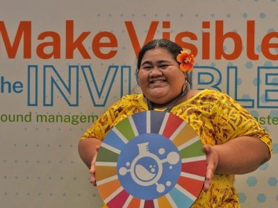 Woman holding a circular symbol behind a "Make Visible the Invisible" backdrop