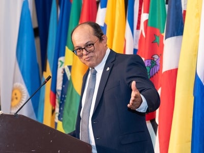 Man gesturing at podium with flags in background