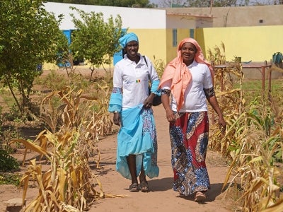 Two smiling Senegalese women walking through a dry corn field